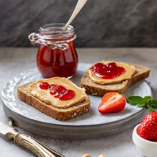 Firefly slices of rye bread with creamy peanut butter and strawberry flavored jelly ready for eat; v