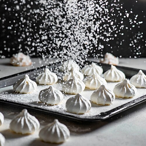 Firefly white meringue kiss cookies on a baking sheet with white confectionary sugar sprinkling on i